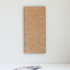 May include: A brown cork board with a textured surface. The board is mounted on a white wall.