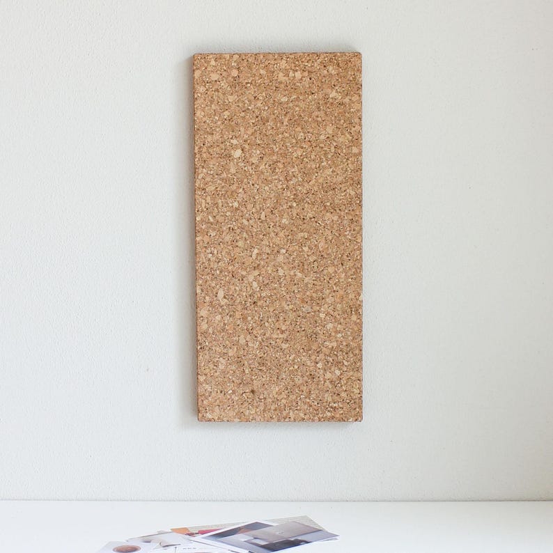 May include: A brown cork board with a textured surface. The board is mounted on a white wall.