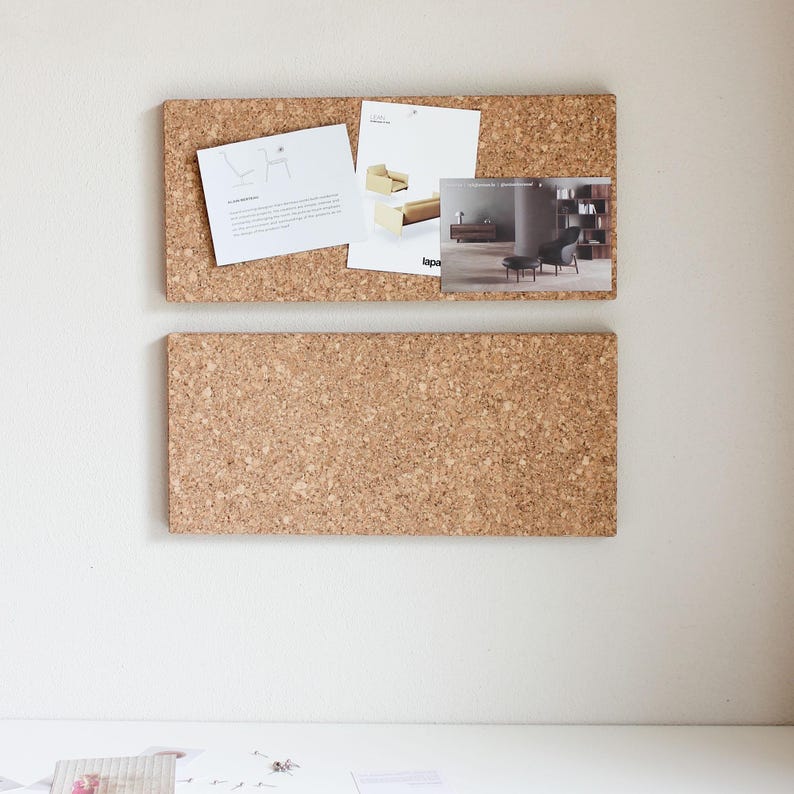 May include: Two cork boards with a tan background. The top board has three pieces of paper with text and images of furniture. The bottom board is empty.