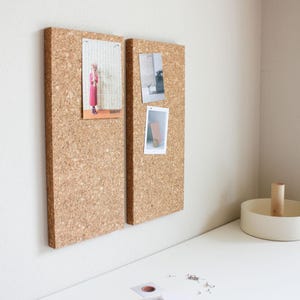 May include: Two cork boards with a light brown finish, mounted on a white wall. The boards are each holding several photos, including a photo of a person wearing a red dress and a photo of a wooden object.