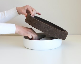 May include: A white ceramic bowl with a brown cork lid. The lid is slightly ajar, revealing the interior of the bowl.