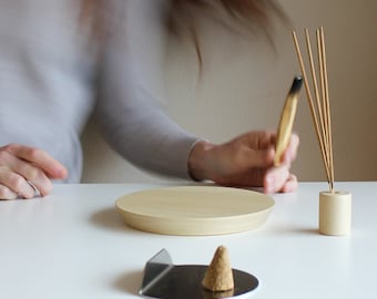 Könnte beinhalten: Ein hölzerner Räucherstäbchenhalter mit runder Basis und einem kleinen Kegel-Räucherstäbchenbrenner. Ein Bündel Räucherstäbchen wird in den Halter gelegt. Die Räucherstäbchen sind angezündet und der Rauch steigt auf.