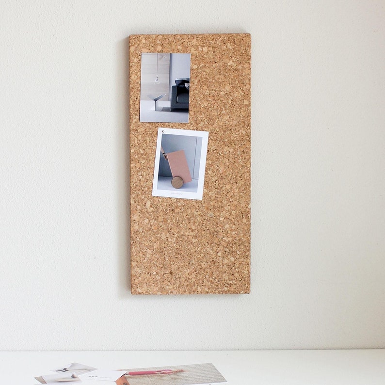 May include: A corkboard with two photos pinned to it. The photos are in black and white and show a room with a couch and a small table, and a small cart with a wooden wheel.