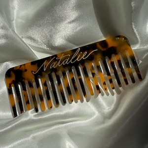 Puede incluir: Un peine de carey con vetas negras y marrones. El peine tiene una inscripción personalizada que dice "Natalie".