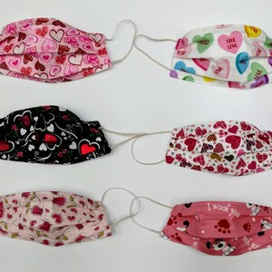 May include: Six different fabric face masks with various heart-themed patterns. The masks are pink, white, black, and red with hearts, candy hearts, and paw prints.
