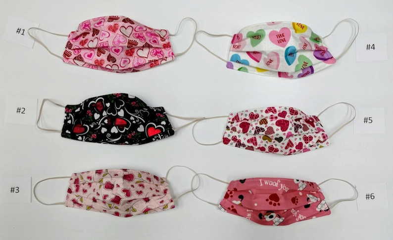May include: Six different fabric face masks with various heart-themed patterns. The masks are pink, white, black, and red with hearts, candy hearts, and paw prints.
