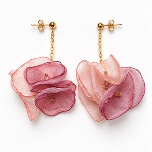 May include: A pair of gold-tone stud earrings featuring dangling chains attached to layered, semi-sheer fabric petals in shades of light pink, magenta, and deep purple. Each earring includes a small gold bead accent at the center of the petals.