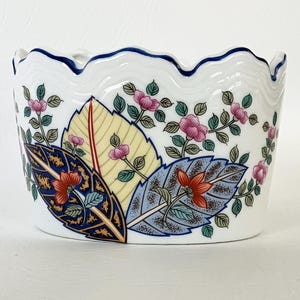 May include: White ceramic bowl with a scalloped rim and a blue trim. The bowl is decorated with colorful floral and leaf patterns in shades of pink, yellow, blue, and orange. A decorative piece for the home.