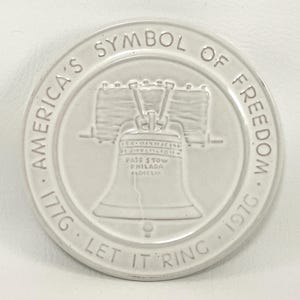 May include: White ceramic coaster with a raised image of the Liberty Bell. The text around the bell reads "America's Symbol of Freedom 1776 Let It Ring 1976".