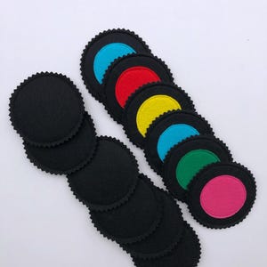 May include: A collection of felt coasters in a retro vinyl record design. The coasters are black with colorful center circles in blue, red, yellow, green, and pink. The edges have a scalloped design.
