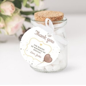 May include: A white round favour tag with gold and pink accents. The tag features a heart-shaped balloon with a string and the text "Thank you" in a cursive font. The text inside the frame reads "For making my birthday so special! Love, Justin".