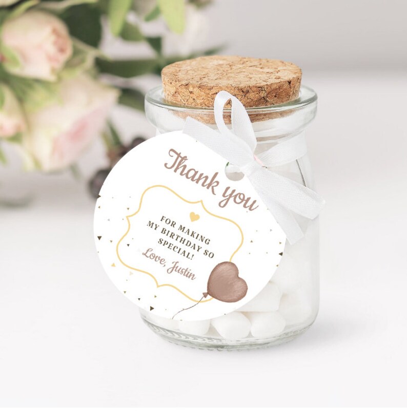 May include: A white round favour tag with gold and pink accents. The tag features a heart-shaped balloon with a string and the text "Thank you" in a cursive font. The text inside the frame reads "For making my birthday so special! Love, Justin".