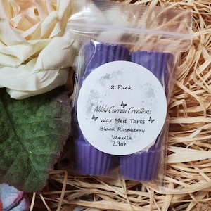 May include: An 8-pack of purple wax melt tarts in a clear plastic bag. The label reads "Nikki Curran Creations Wax Melt Tarts Black Raspberry Vanilla 2.3 oz."