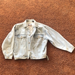 May include: A light blue denim jacket with two front pockets and a button closure.