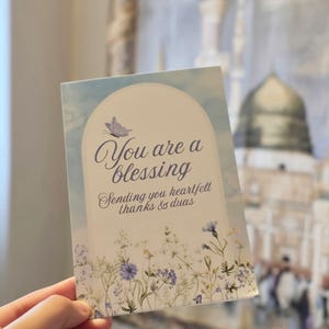 May include: A rectangular greeting card featuring a light blue sky background with a white archway. The text reads You are a blessing and Sending you heartfelt thanks & duas. A small purple butterfly and a field of blue and yellow wildflowers are printed.