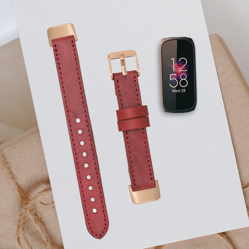 May include: Two red leather watch bands with gold hardware. The bands are shown on a white surface with a black smartwatch displaying the time 12:58 and the date Wed 28.