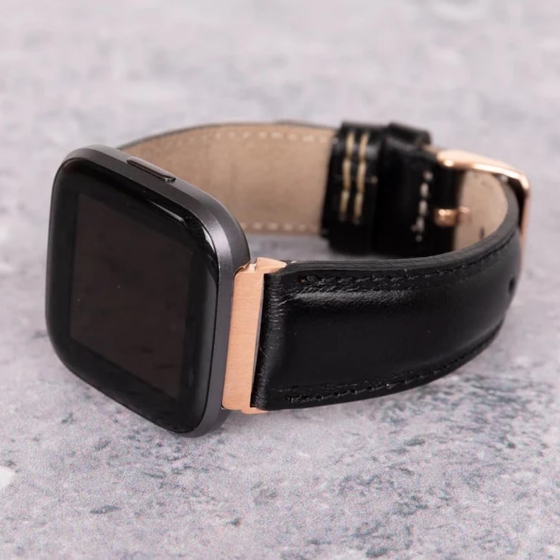 Peut inclure: Un bracelet de montre en cuir noir avec une boucle en or rose et un cadran de montre noir. Le bracelet est cousu de blanc.
