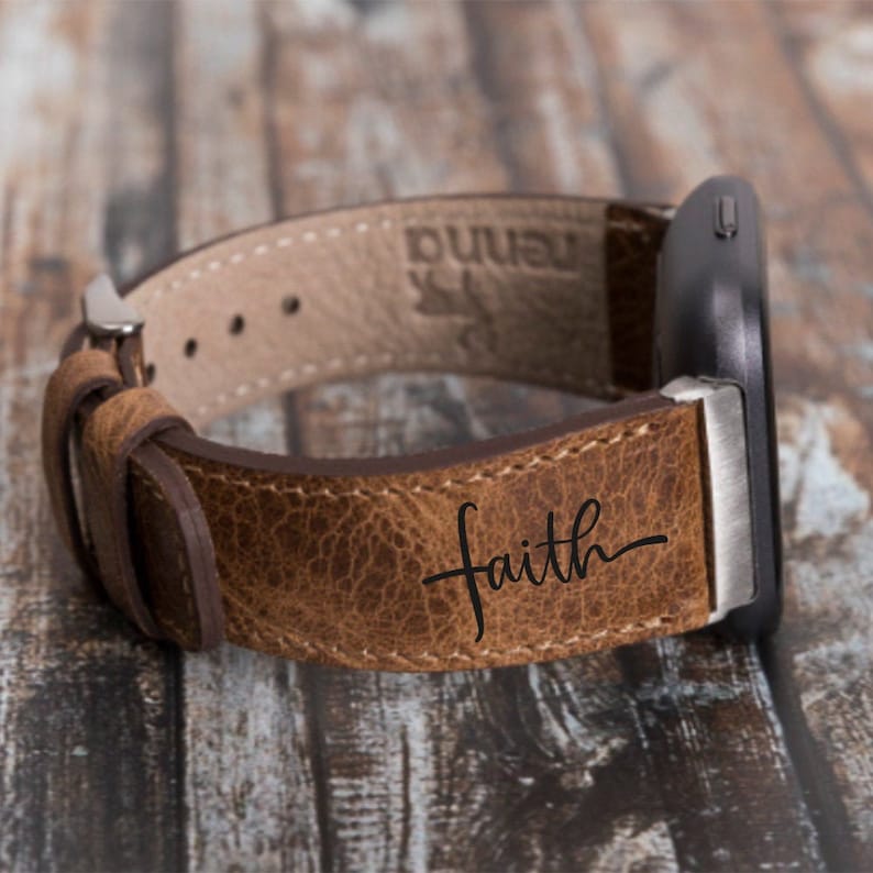 Puede incluir: Una correa de reloj de cuero marr&oacute;n con la palabra "faith" grabada en escritura cursiva.