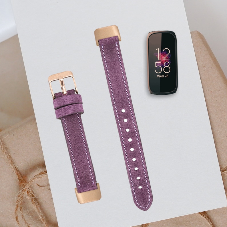 May include: Two purple leather watch bands with gold hardware. The band on the left has a buckle and the band on the right has a pointed end. The watch face shows the time 12:58 and the date Wed 28.