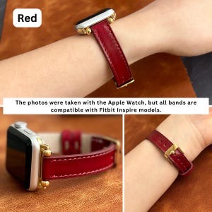 May include: Red leather watch band with gold hardware. The band is shown on a wrist and on a table.
