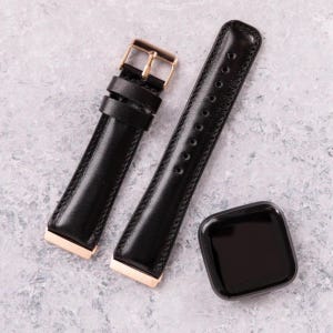 Peut inclure: Deux bracelets de montre en cuir noir avec des d&eacute;tails en or rose. Les bracelets sont sur une surface gris clair.