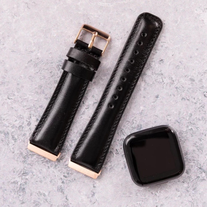 Peut inclure: Deux bracelets de montre en cuir noir avec des d&eacute;tails en or rose. Les bracelets sont sur une surface gris clair.