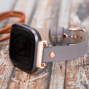 May include: A gray leather watch band with rose gold accents and a black smartwatch.