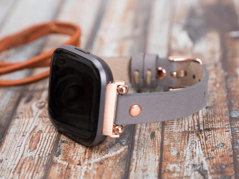 May include: A gray leather watch band with rose gold accents and a black smartwatch.