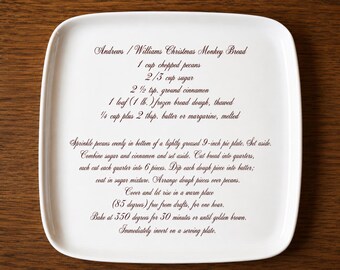 May include: A square white ceramic plate with rounded corners featuring dark brown printed text of the Andrews / Williams Christmas Monkey Bread recipe, including ingredients like 1 cup chopped pecans and instructions for a 9-inch pie plate.