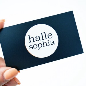 May include: A black business card with a white circle in the center. The circle contains the text "halle sophia" in black.