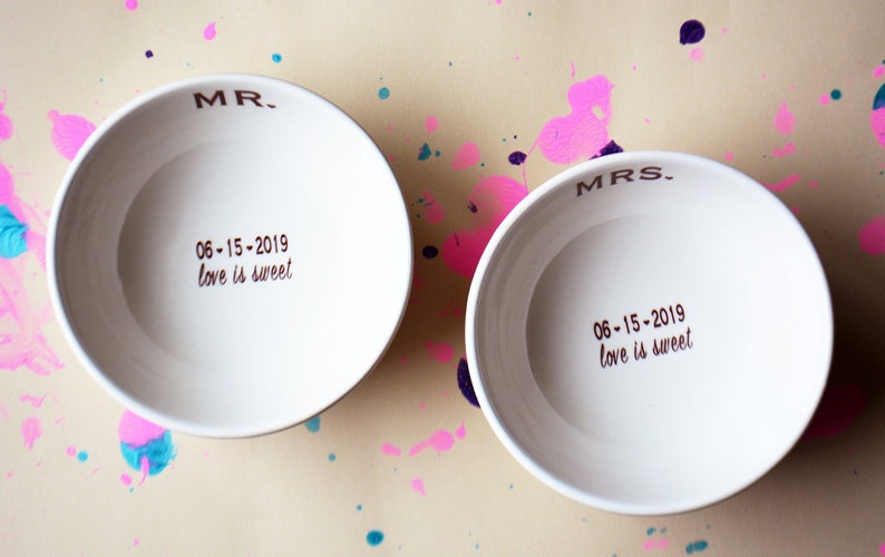 May include: Two white ceramic bowls with the words "MR." and "MRS." written on them. The bowls also have the date "06-15-2019" and the phrase "love is sweet" written on them.