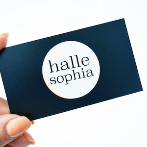 May include: A black business card with a white circle in the center. The circle contains the text "halle sophia" in black.