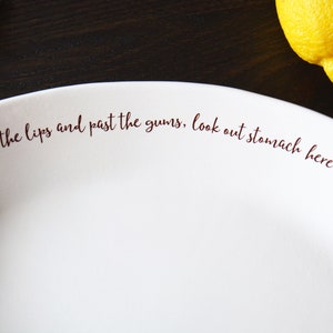May include: White ceramic plate with the text "Over the lips and past the gums, look out stomach here it comes." printed in brown.