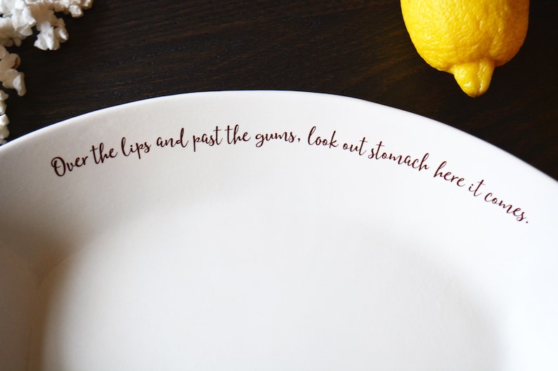 May include: White ceramic plate with the text "Over the lips and past the gums, look out stomach here it comes." printed in brown.
