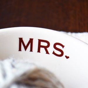May include: White ceramic bowl with the word "MRS." printed in red lettering with a small red heart.
