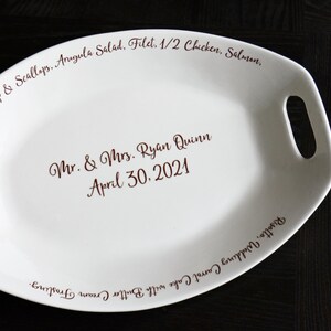 May include: White oval serving platter with handles. The platter is personalized with the text "Shrimp & Scallops, Arugula Salad, Filet, 1/2 Chicken, Salmon, Mr. & Mrs. Ryan Quinn April 30. 2021" and "Risotto, Wedding Carrot Cake with Butter Cream Frosting."