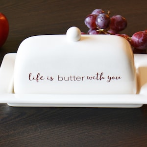 May include: White ceramic butter dish with a lid and a red inscription that reads "life is butter with you".