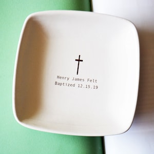 Puede incluir: Plato de cerámica blanco con una cruz y el texto "Henry James Felt Bautizado 12.15.19".