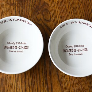 May include: Two white ceramic bowls with the text "MR. WILKINSON" and "MRS. WILKINSON" on the rim. The bowls have the text "Chantz & Valeria ENGAGED 03-23-2025 love is sweet" printed on the bottom.