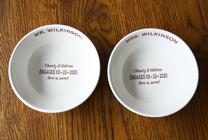 May include: Two white ceramic bowls with the text "MR. WILKINSON" and "MRS. WILKINSON" on the rim. The bowls have the text "Chantz & Valeria ENGAGED 03-23-2025 love is sweet" printed on the bottom.