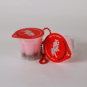 May include: Two clear plastic cups with pink contents and a dark brown base, each topped with a red lid. The lids feature white text and a logo. A red beaded chain connects the cups. The text on the lid says "STRAY KIDS EVERYWHERE ALL AROUND THE WORLD".