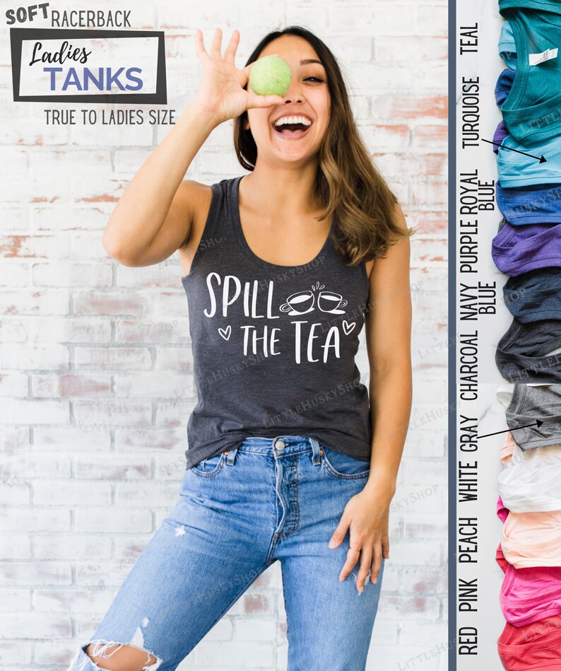May include: A woman wearing a gray tank top with the text "Spill the Tea" and two teacup illustrations. The tank top is available in a variety of colors, including red pink, peach, white, gray, charcoal, navy, purple, royal, turquoise, and teal.