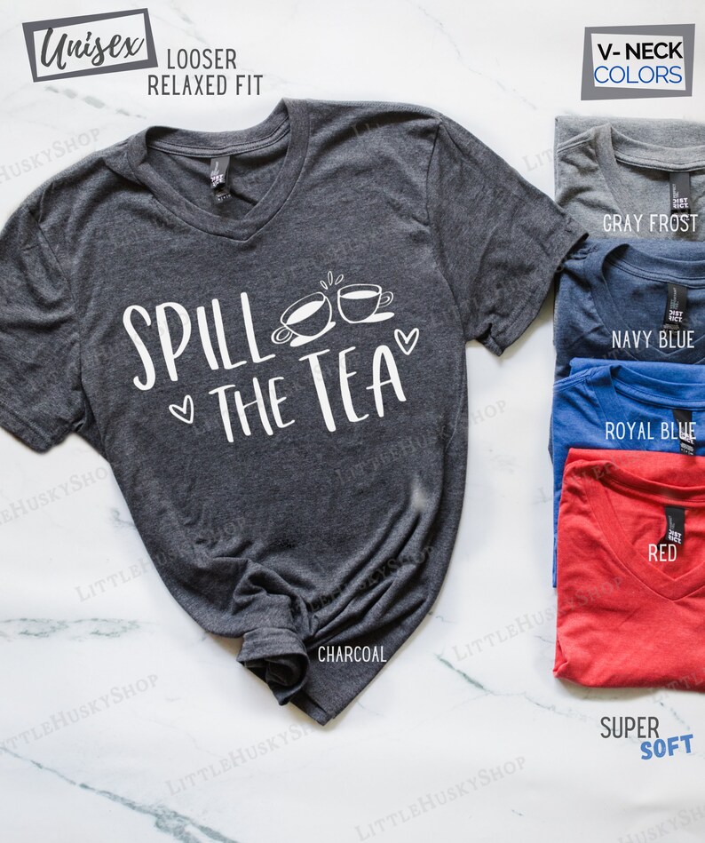 May include: A charcoal gray V-neck t-shirt with the text "Spill the Tea" in white. The shirt has a relaxed fit and is available in other colors, including gray frost, navy blue, royal blue, and red.