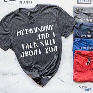 Puede incluir: Una camiseta de cuello en V gris antracita con el texto "My Dachshund and I Talk Shit About You" impreso en blanco. La camiseta est&aacute; disponible en otros colores, incluyendo gris escarcha, azul marino, azul real y rojo.