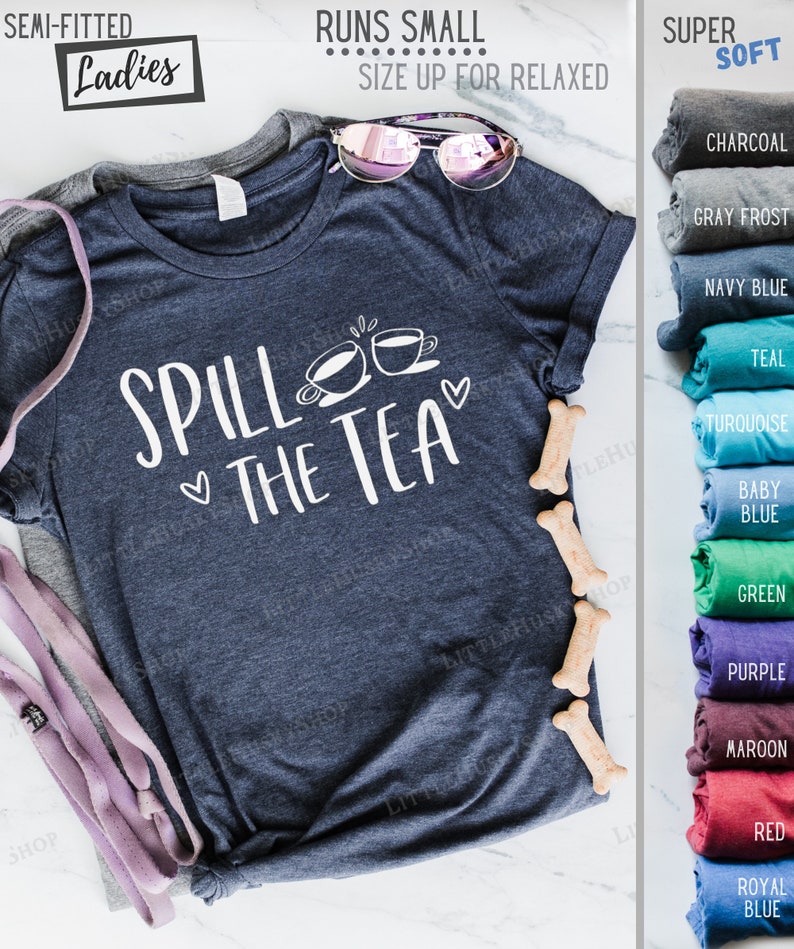 May include: A navy blue t-shirt with the text "Spill the Tea" and two teacups. The shirt is semi-fitted and runs small. The shirt is available in a variety of colors, including charcoal, gray frost, navy blue, teal, turquoise, baby blue, green, purple, maroon, red, and royal blue.
