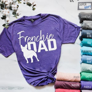 May include: A purple unisex t-shirt with the words "Frenchie Dad" in white, along with a white silhouette of a French Bulldog. The shirt is labeled "Super Soft" and has a variety of color options displayed.