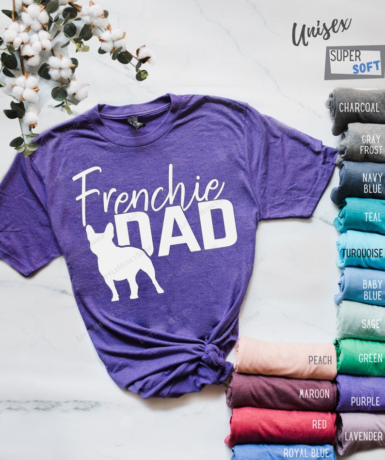 May include: A purple unisex t-shirt with the words "Frenchie Dad" in white, along with a white silhouette of a French Bulldog. The shirt is labeled "Super Soft" and has a variety of color options displayed.