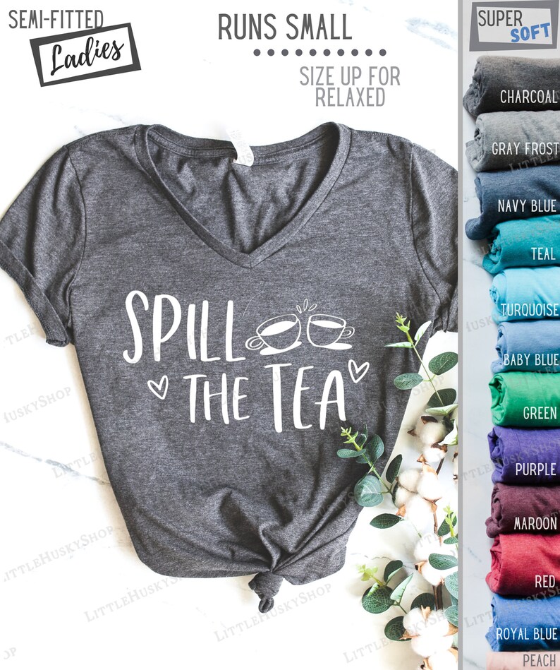 May include: A heather gray V-neck t-shirt with the text "Spill the Tea" in white lettering. Two white teacup illustrations are above the text. The shirt is semi-fitted and runs small. The text "Super Soft" is in a white box in the upper right corner of the image. The image shows a variety of colors for the shirt, including charcoal, gray frost, navy blue, teal, turquoise, baby blue, green, purple, maroon, red, royal blue, and peach.