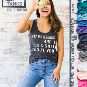 Puede incluir: Una mujer lleva una camiseta sin mangas gris con el texto "My Dachshund and I Talk Shit About You" en blanco. Est&aacute; sosteniendo una manzana verde frente a su cara y sonriendo. La camiseta sin mangas est&aacute; disponible en una variedad de colores, incluyendo rosa rojo, melocot&oacute;n, blanco, gris, carb&oacute;n, azul marino, morado, azul real, turquesa y azul verdoso.