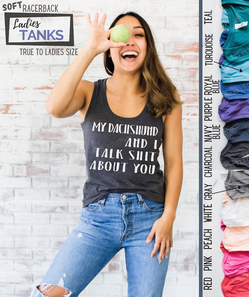 Puede incluir: Una mujer lleva una camiseta sin mangas gris con el texto "My Dachshund and I Talk Shit About You" en blanco. Est&aacute; sosteniendo una manzana verde frente a su cara y sonriendo. La camiseta sin mangas est&aacute; disponible en una variedad de colores, incluyendo rosa rojo, melocot&oacute;n, blanco, gris, carb&oacute;n, azul marino, morado, azul real, turquesa y azul verdoso.